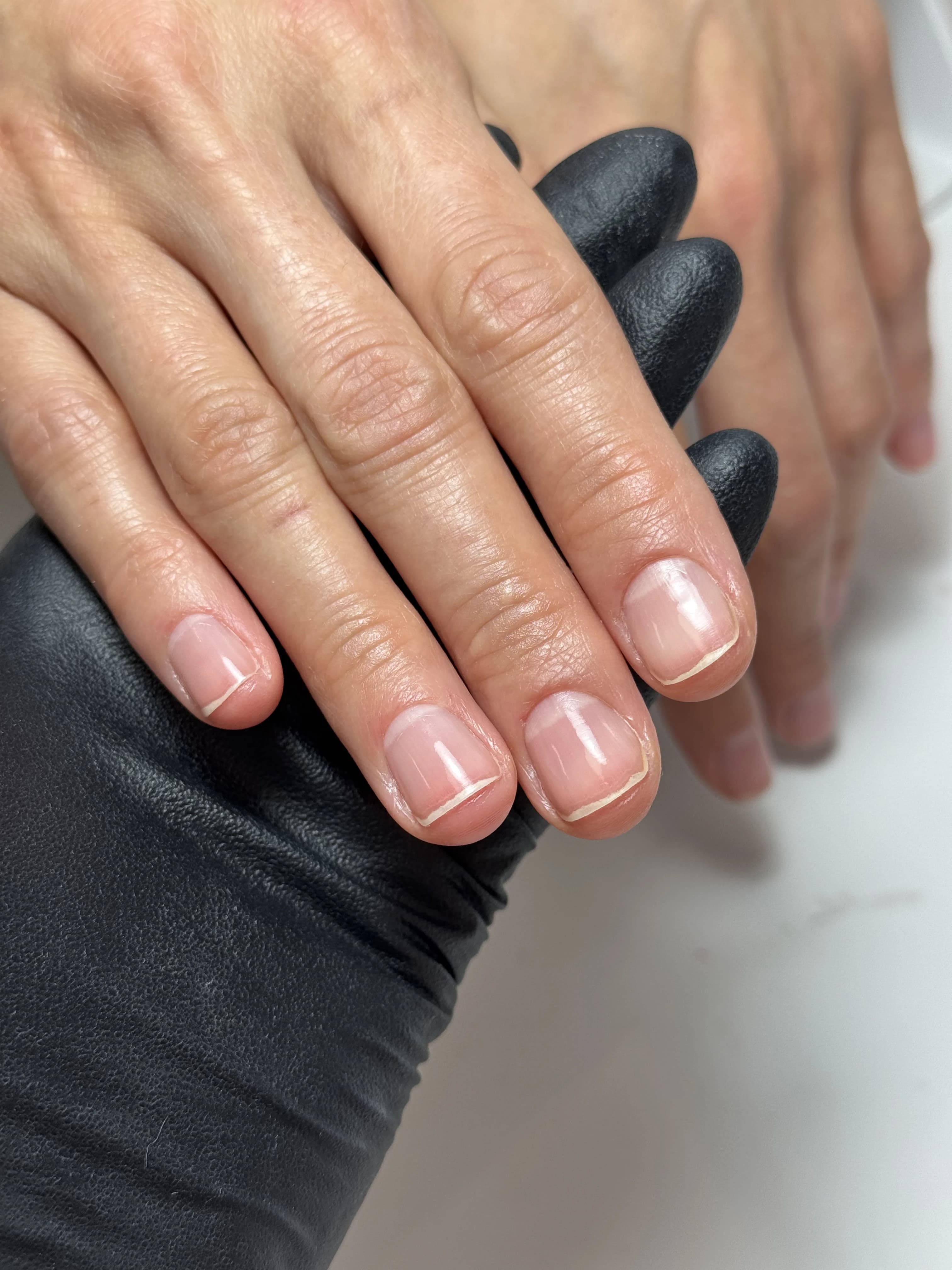 Glass-like Japanese manicure shine on short natural nails as a Mississauga tech in black gloves holds the hand.